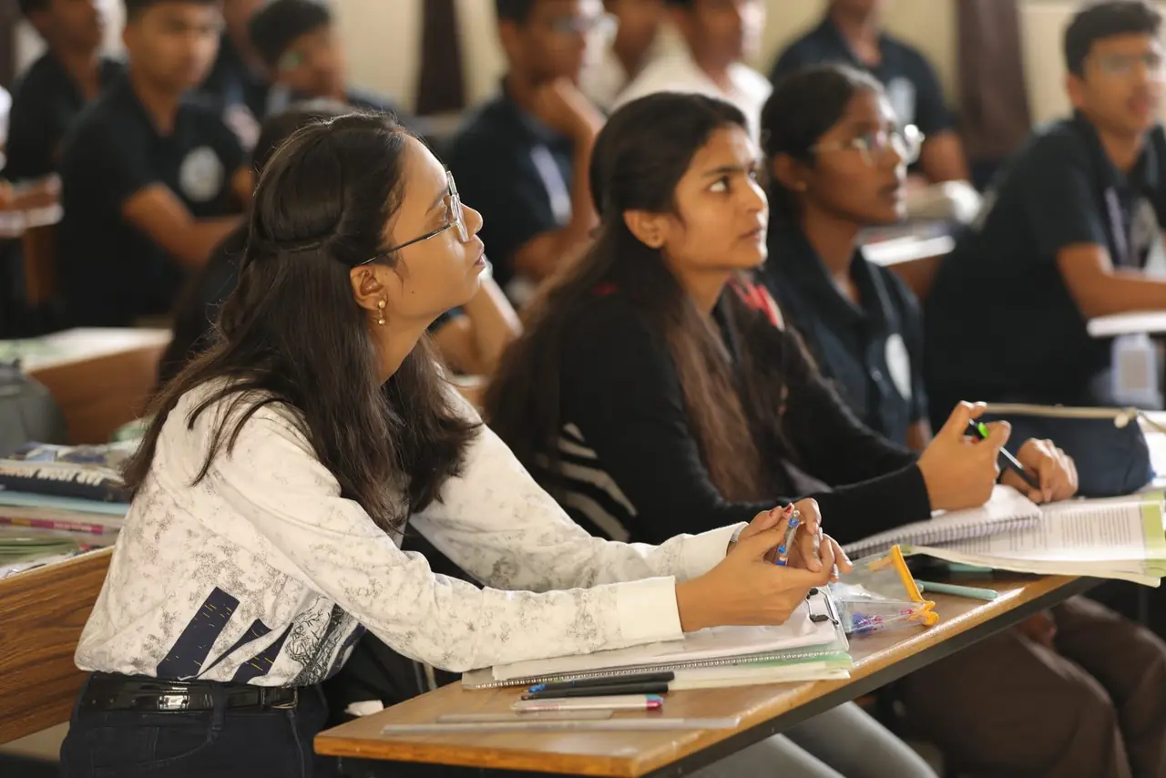 Two PUC students listening closely in a NEET class, pens in hand